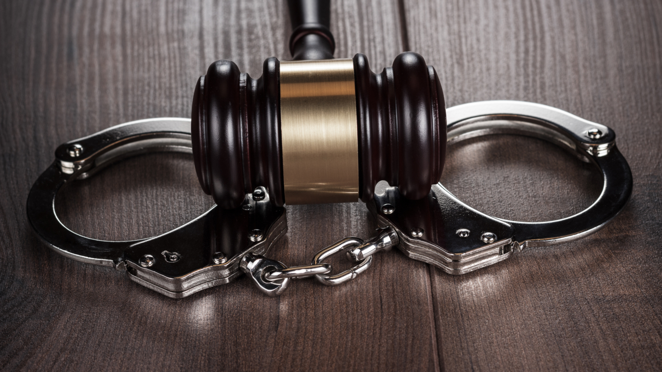 handcuffs and judge gavel on brown wooden table background
